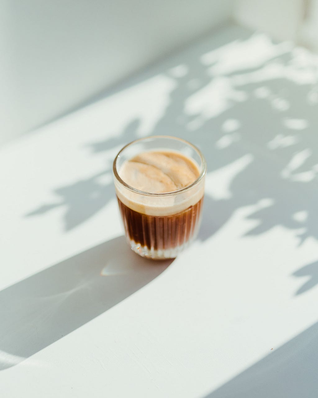 A glass of coffee with thick crema on a white table.