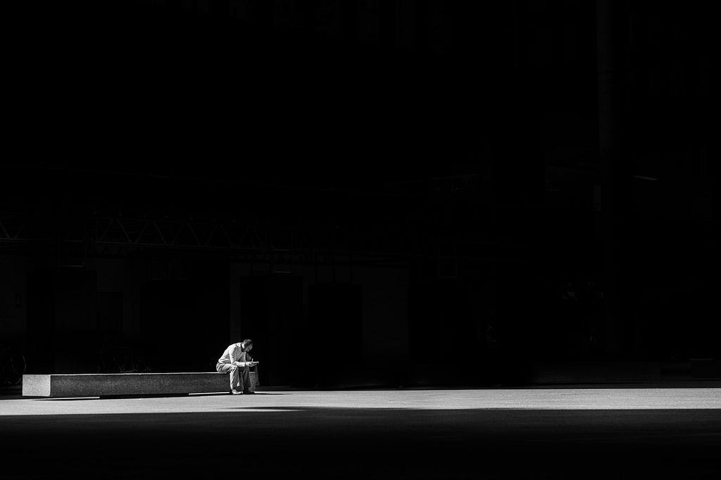 black and white of man sitting alone on bench in large empty space // Photographer: Matthew Henry | Source: Unsplash