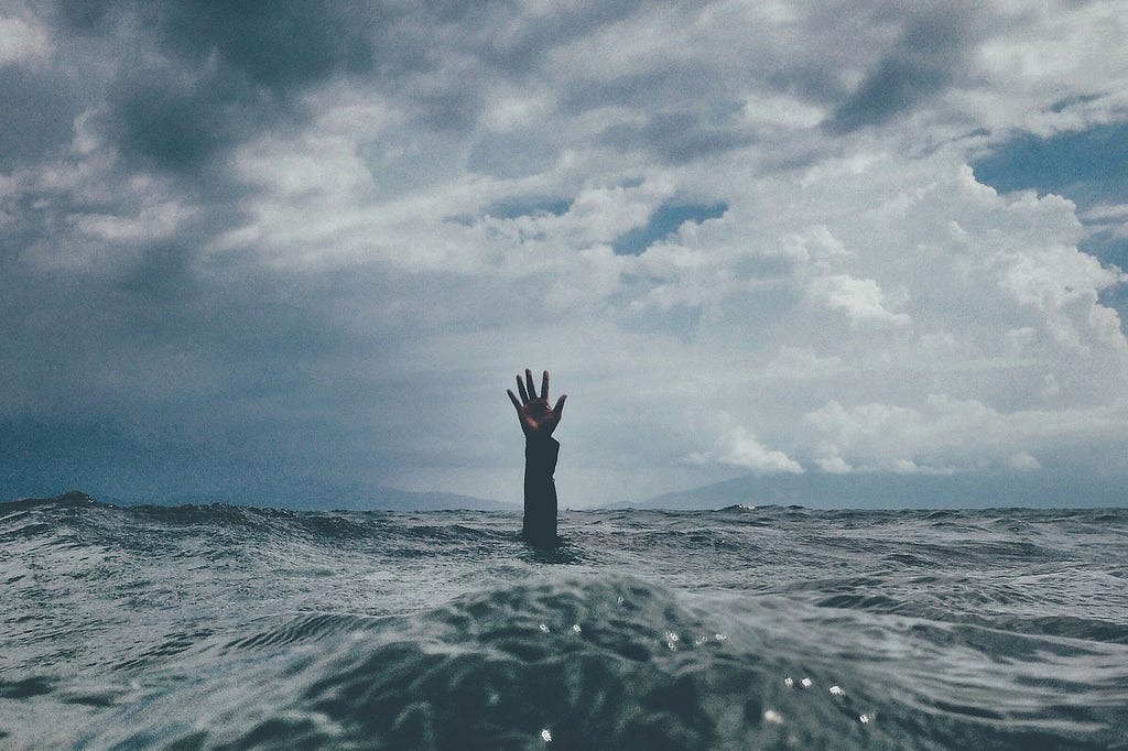 A person under water with just their hand reaching out seeking help