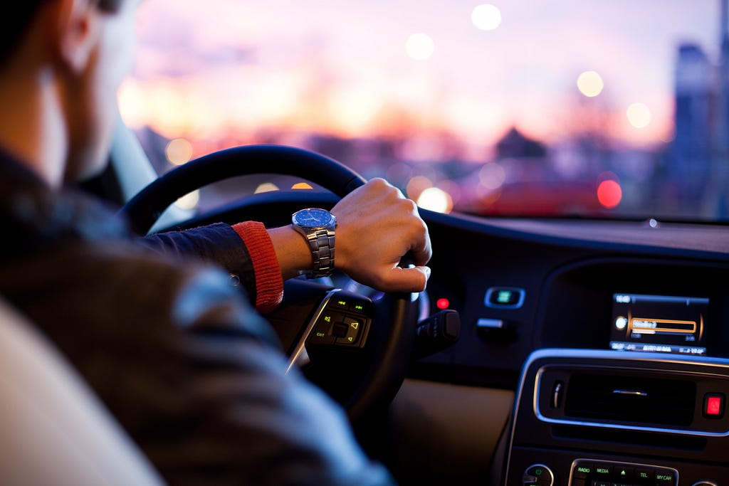 Interior view of a well-dressed individual driving a car at sunset