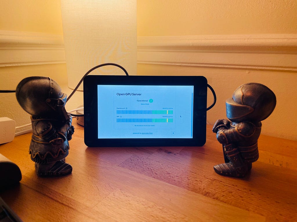 A small tablet or display screen sits on a wooden surface, showing the interface for an “OpenGPU Server” with status bars indicating it’s operational. On either side of the screen are two small figurines of armored guards. The scene is set against the background of a wall with decorative molding, giving it a home-like setting.