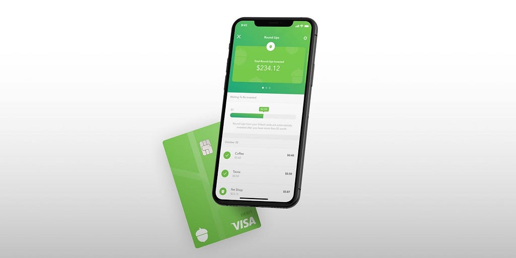 A phone with the Acorns Finance App open. Acorns Visa Debit card behind the phone.
