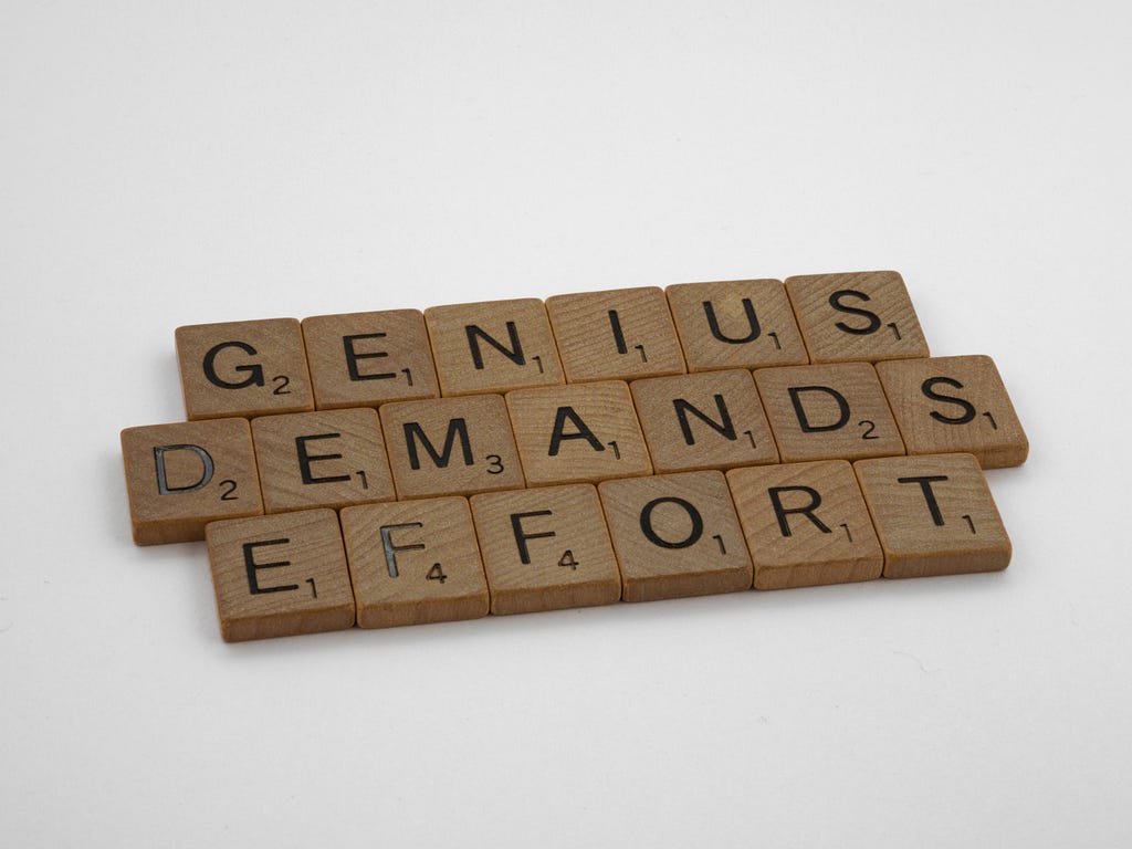 The statement “Genius demands effort” portrayed using scrabble tiles.