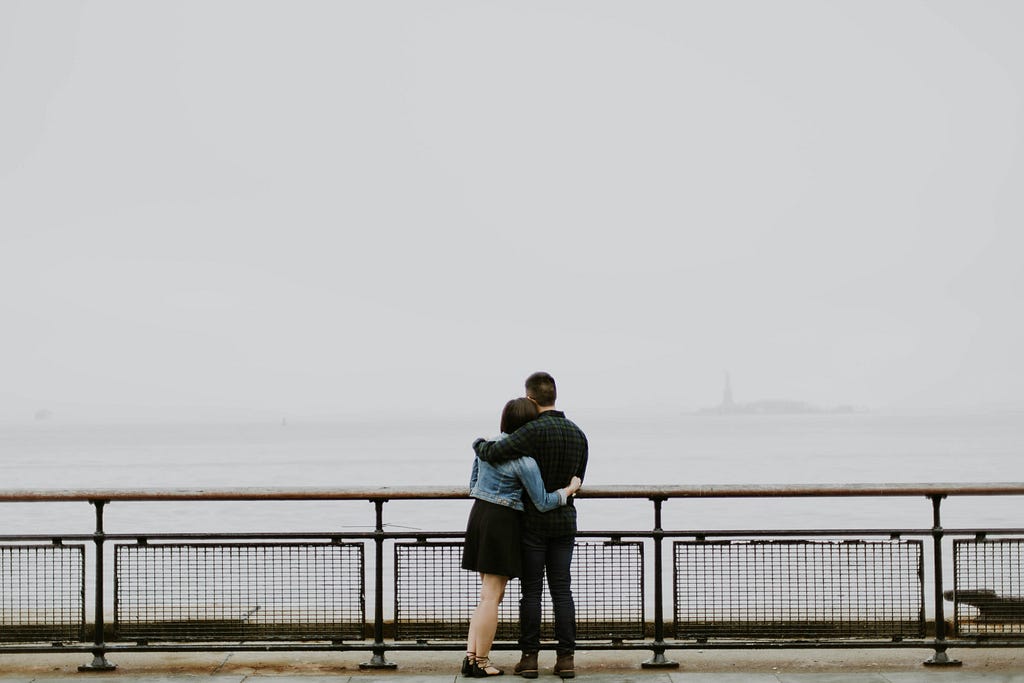 a couple holding each other on a bridge looking out into the foggy sea