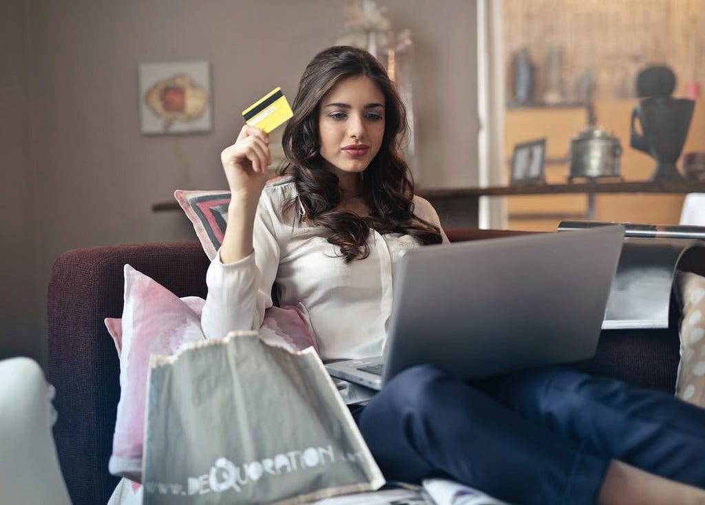 A person is seated using a laptop. They are holding up a credit card and appear to be making an online purchase.