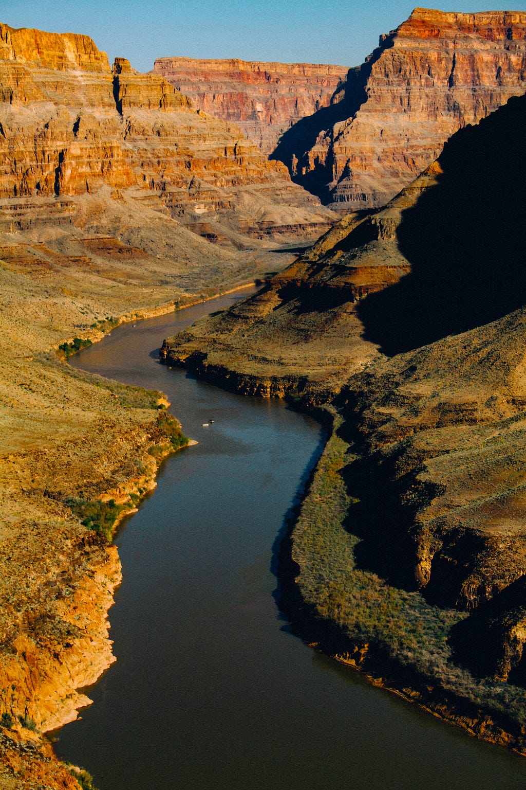 Photo of a large canyon with a river running along the bottom. Layers of different rock are visible in the sides of the canyon