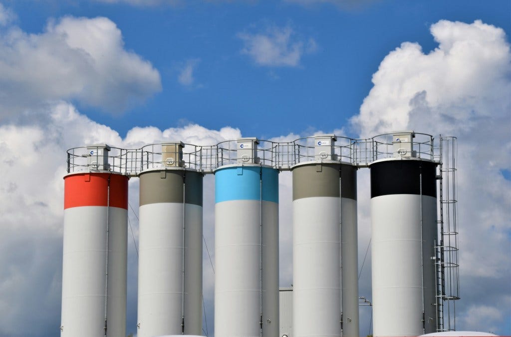 A line of silos, each with a band of color at the top. Red, grey, blue, grey, black.