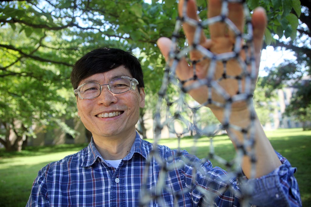 Ming Zheng poses outdoors holding a model of a carbon nanotube, which looks like an open tube made of smaller tubes.