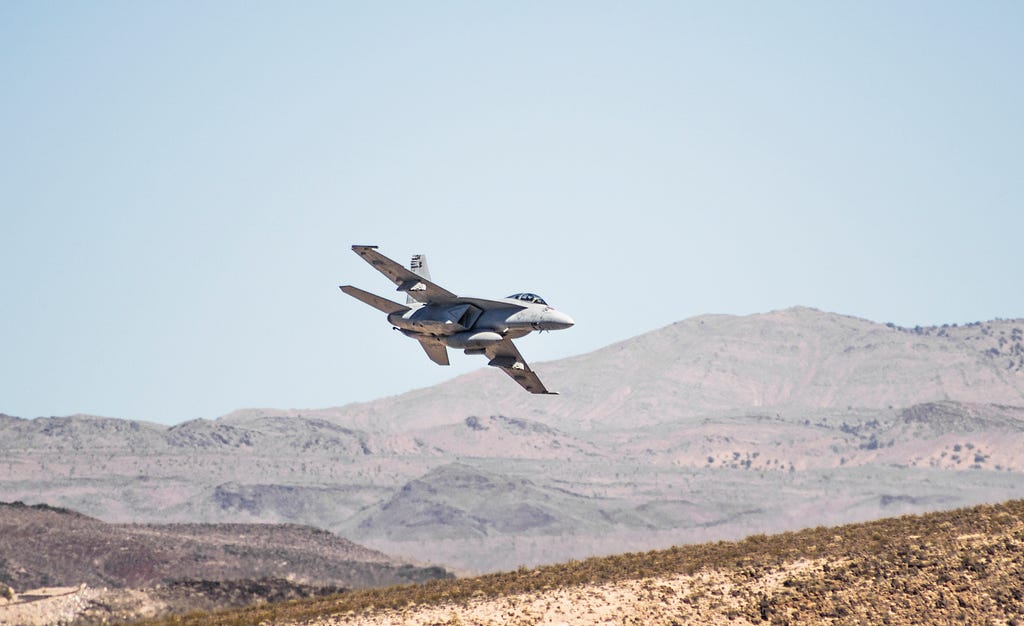 F-18 Hornet Navy fighter airplane over a desert landscape.