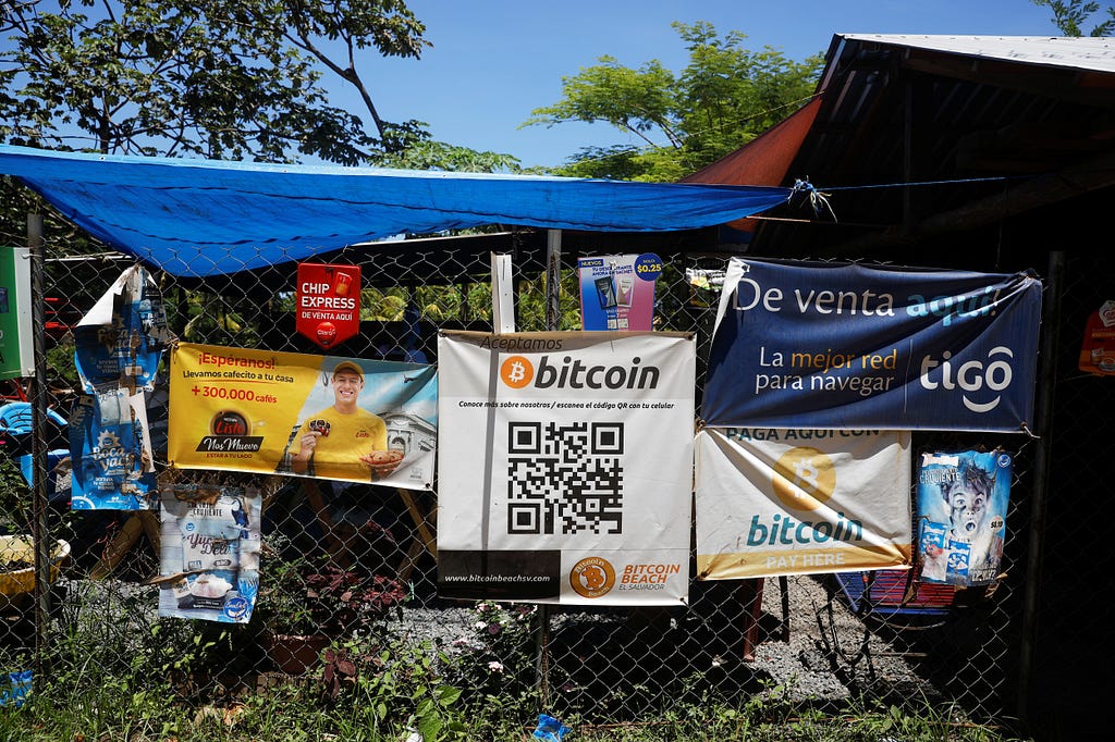 The side of a shopfront in El Salvador is covered in numerous posters, one of which advertises Bitcoin as a payment method.