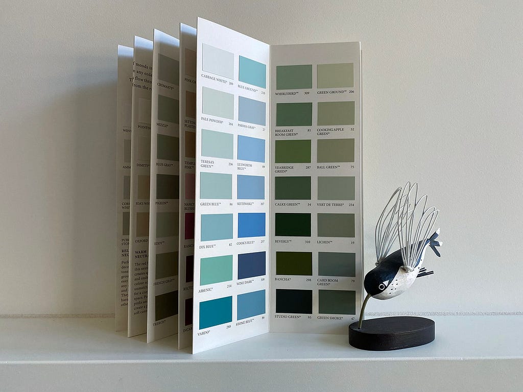 Showing a paint chart, all blues and greens, resting on a mantelpiece next to a model of a hummingbird