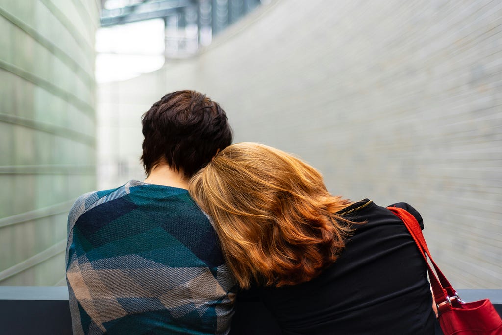 Red headed woman leaning head on companion as they provide support and understanding for a complicated drug addiction.