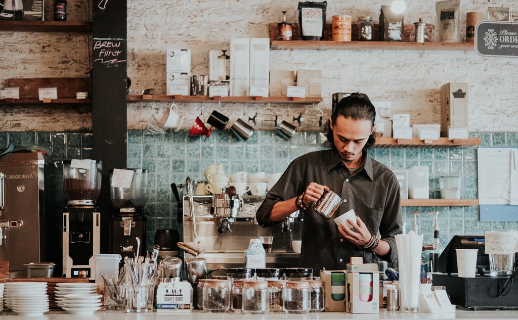 man brewing coffee behind coffee shop counter
