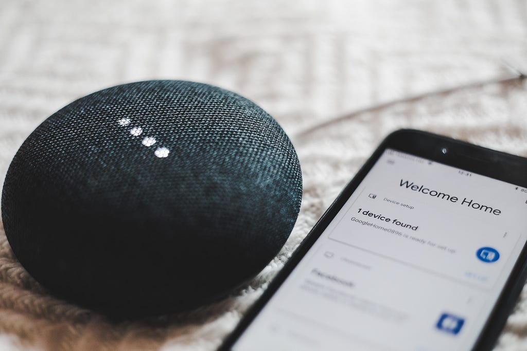 Smart speaker next to a cell phone with screen saying “Welcome Home”