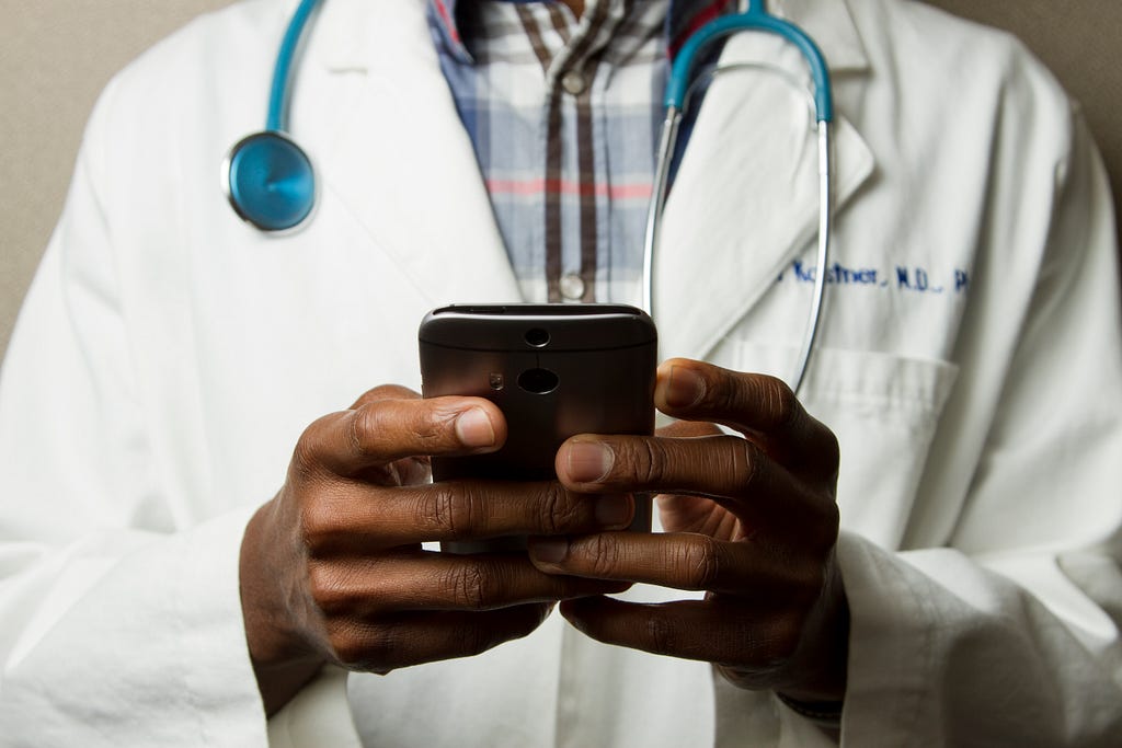 Médico segurando um smartphone, close nas suas mãos segurando o aparelho.