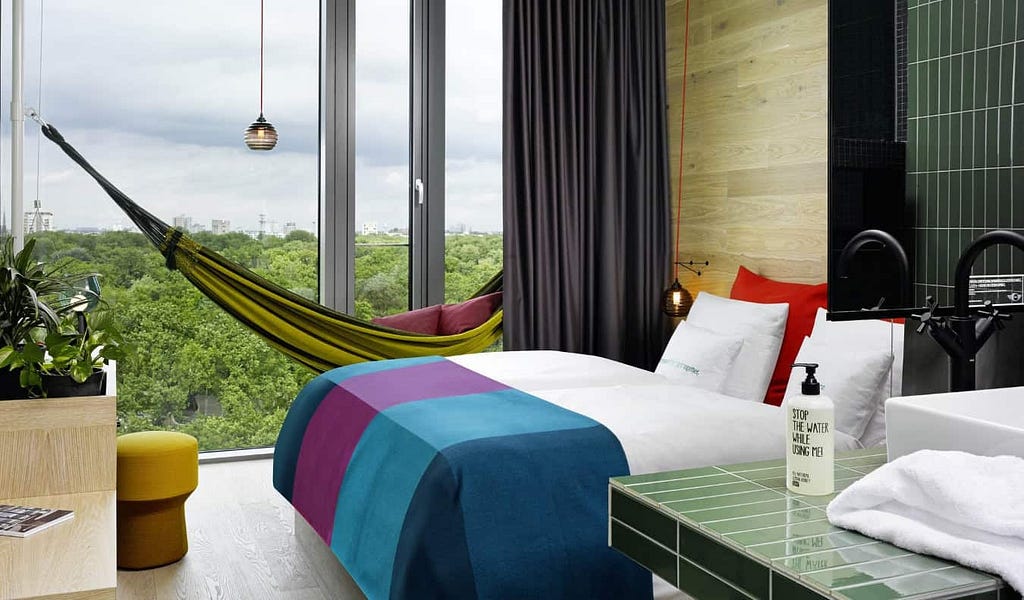 A hotel room with a hammock by the floor-to-ceiling windows and a bed with a bright duvet at 25Hours Bikini, a hotel in Berlin, Germany