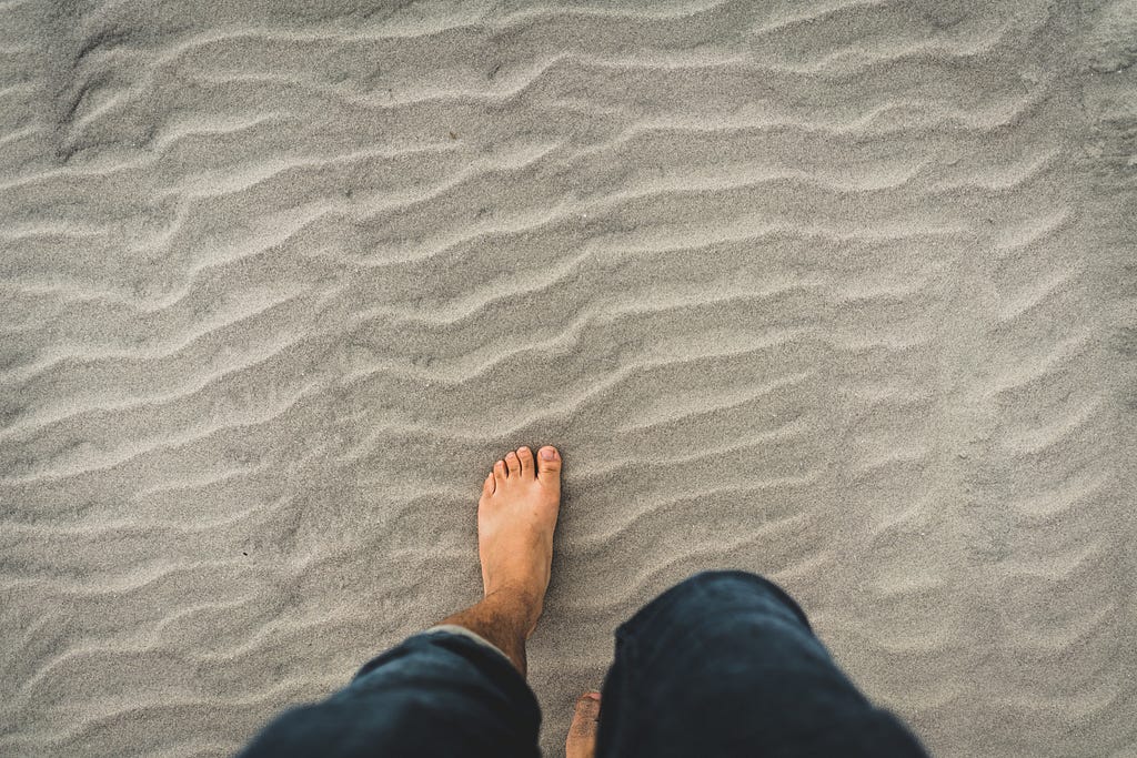 Feet on rippled sand, wearing blue jeans