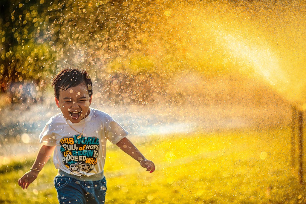 A smiling boy running through a water sprinkler