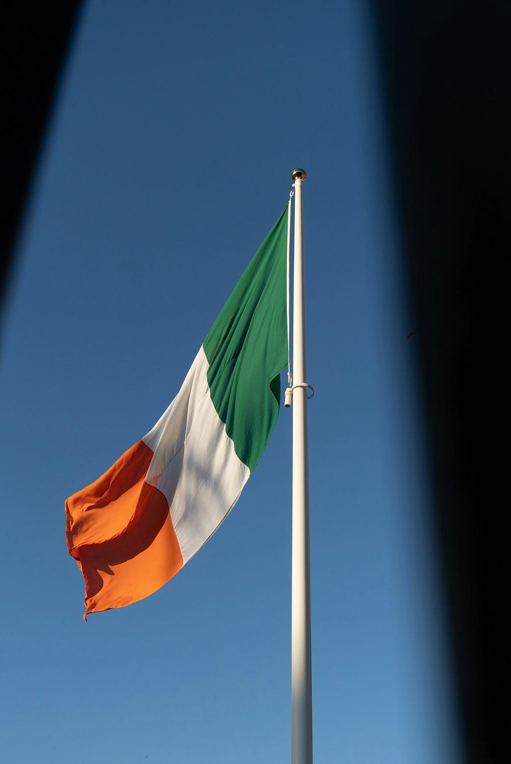 Irish flag (green at the hoist-white-orange in equal ratios) flying against a blue background