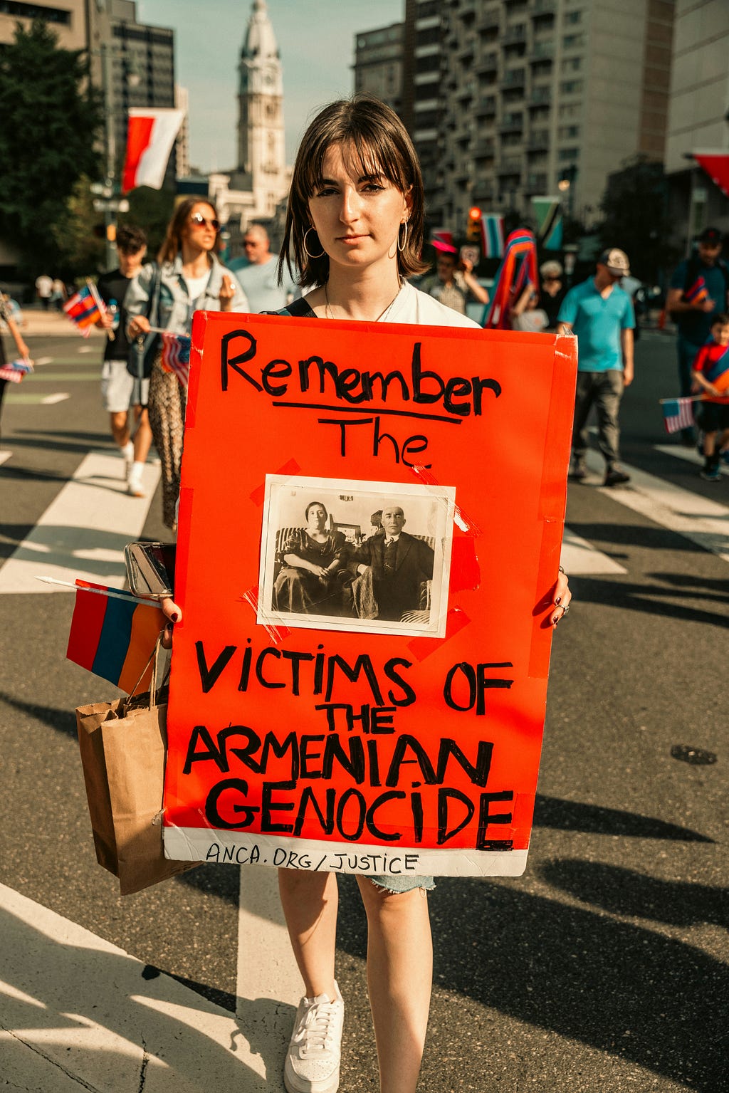 A woman holding a sign at a protest with the words “Remember the Victims of the Armenian Genocide”, a photograph in the centre depicts an older man and woman who are presumably victims of the genocide