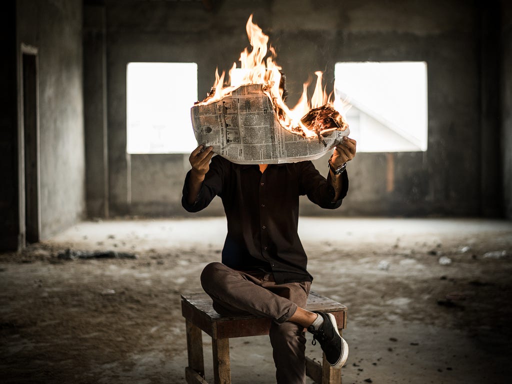 A person in a concrete room, reading a newspaper that’s on fire.