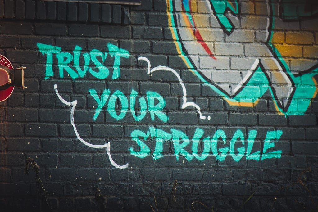 A grafitti-like painting on the wall with the words (in green) saying, “trust your struggle.” To depict the topic’s message about whether or not one should trust the process or whatever it is theyr’e going throug