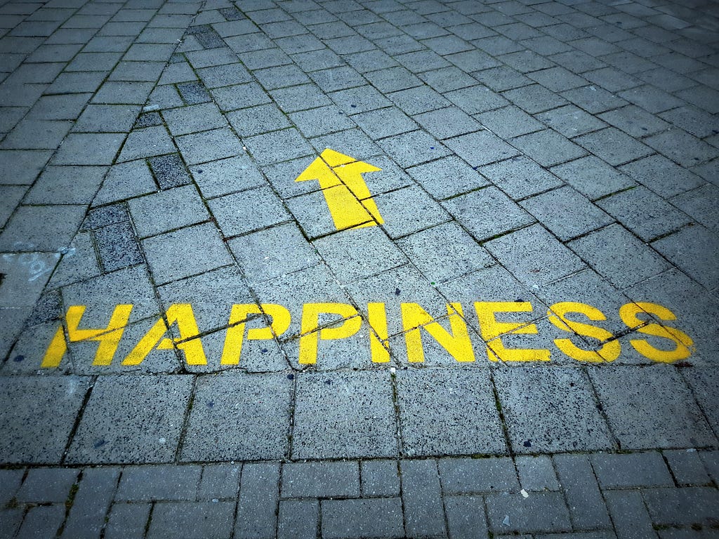 the word “happiness” painted on a pavement, with an arrow pointing forward