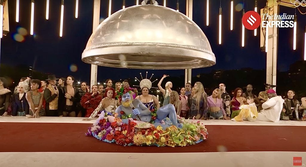 A screenshot of the opening ceremony’s most controversial scene. A half-naked blue man lies on a dinner platter in front of a group of drag queens.