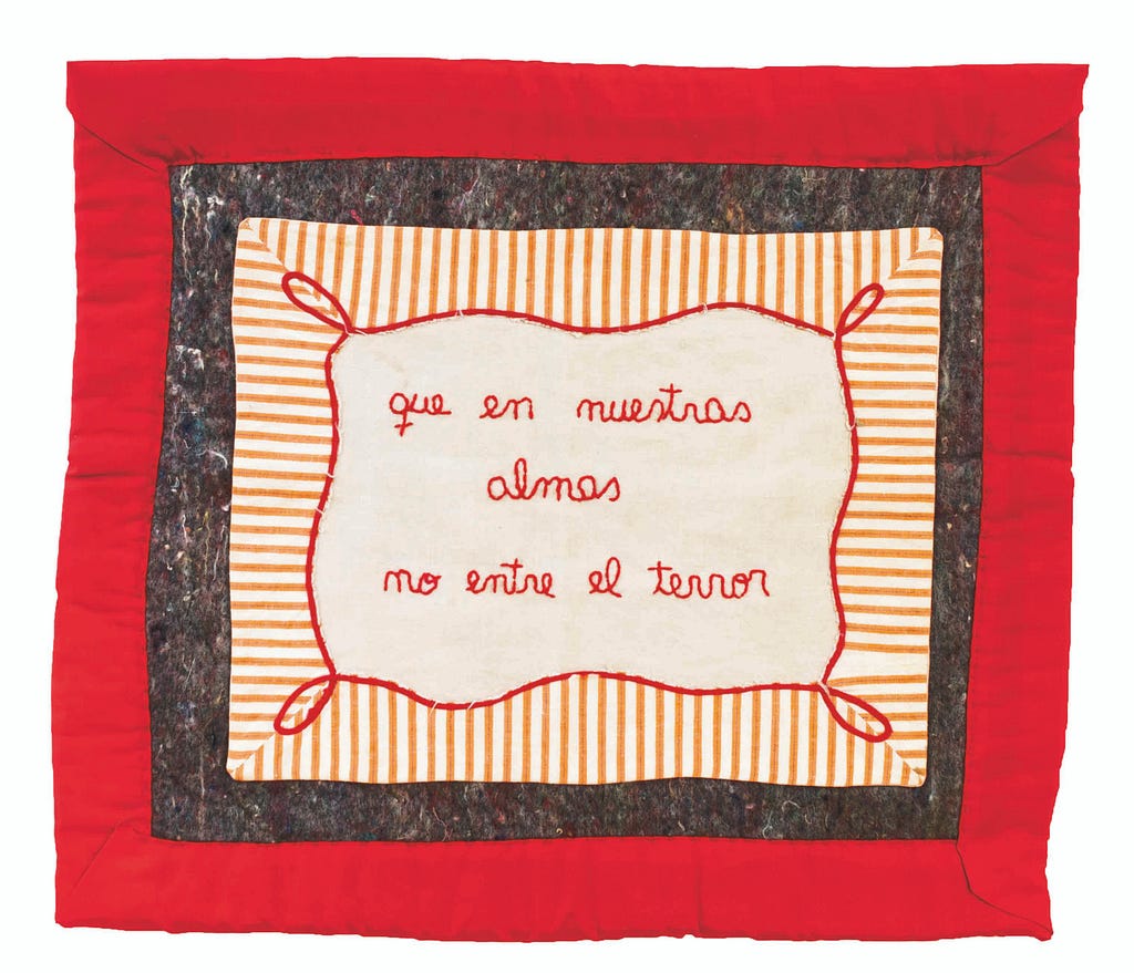 Frazada bordad en rojo con la frase «Que en nuestras almas no entre el terror»