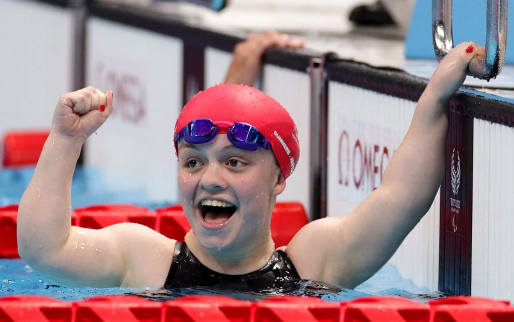 Woman in pool wearing a swim cap and goggles on her head, with arms raised celebrating winning