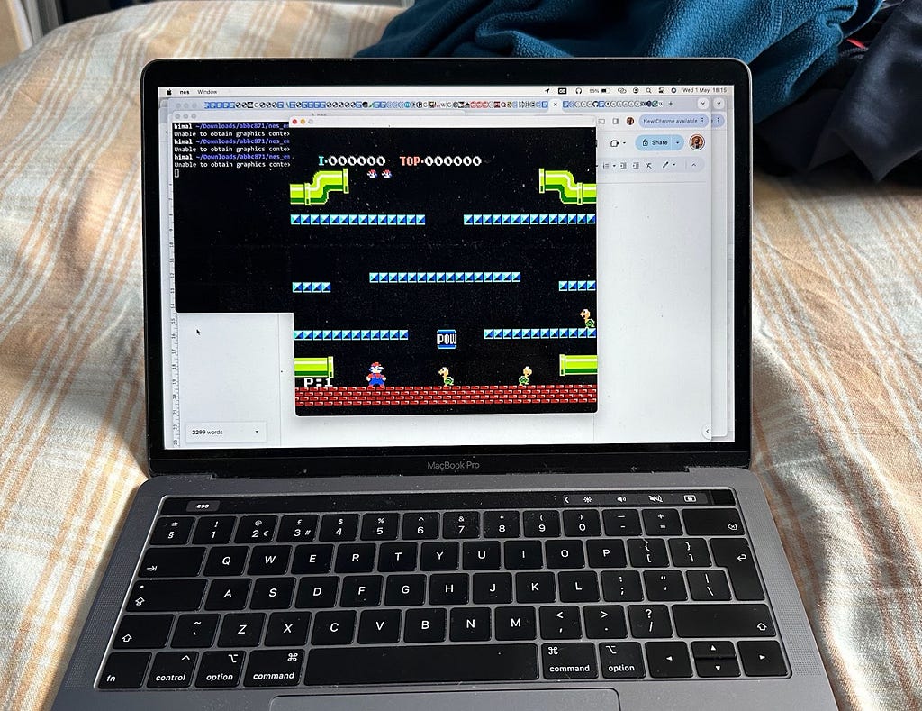 MacBook Pro resting on bed. Screen shows a window running NES Mario Bros game.
