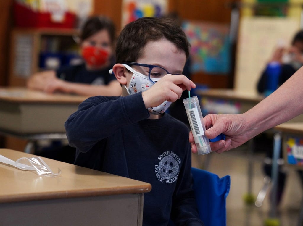 A child places his test swab in a vial at South Boston Catholic Academy in Boston, Massachusetts, January 28, 2021. Photo by Allison Dinner/Reuters