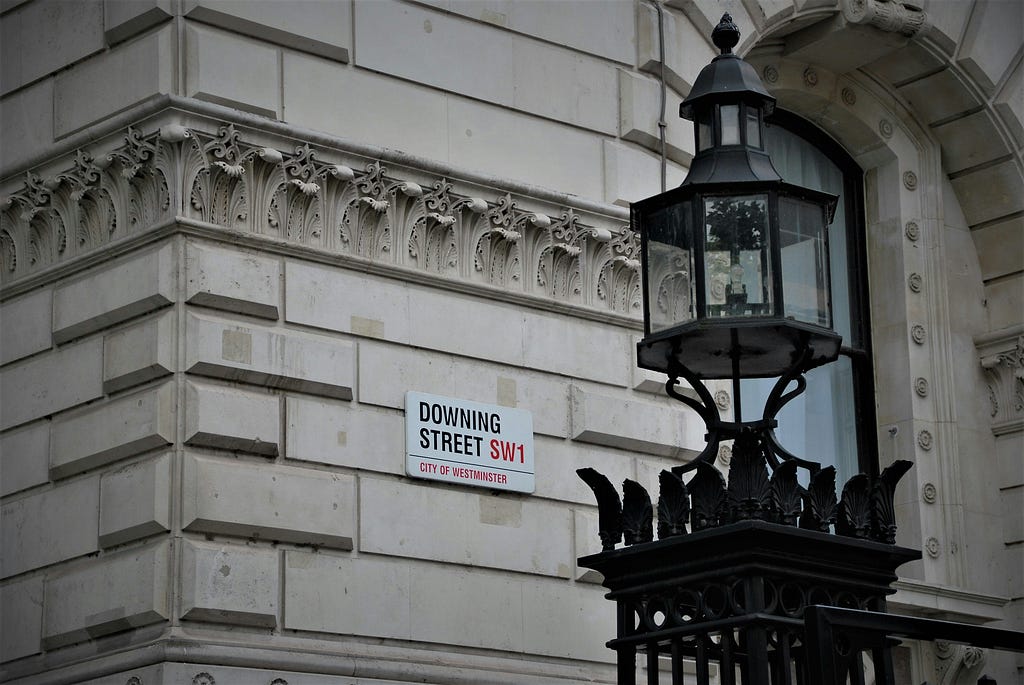 Downing Street sign. On a wall. Ornate black streetlamp in the foreground.
