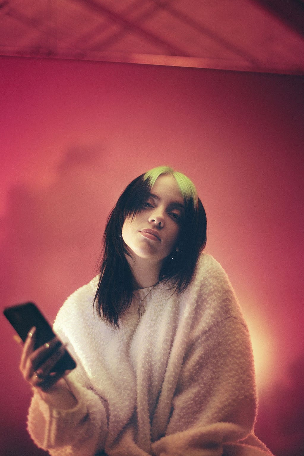 Billie Eilish sitting, holding her phone and staring into the camera