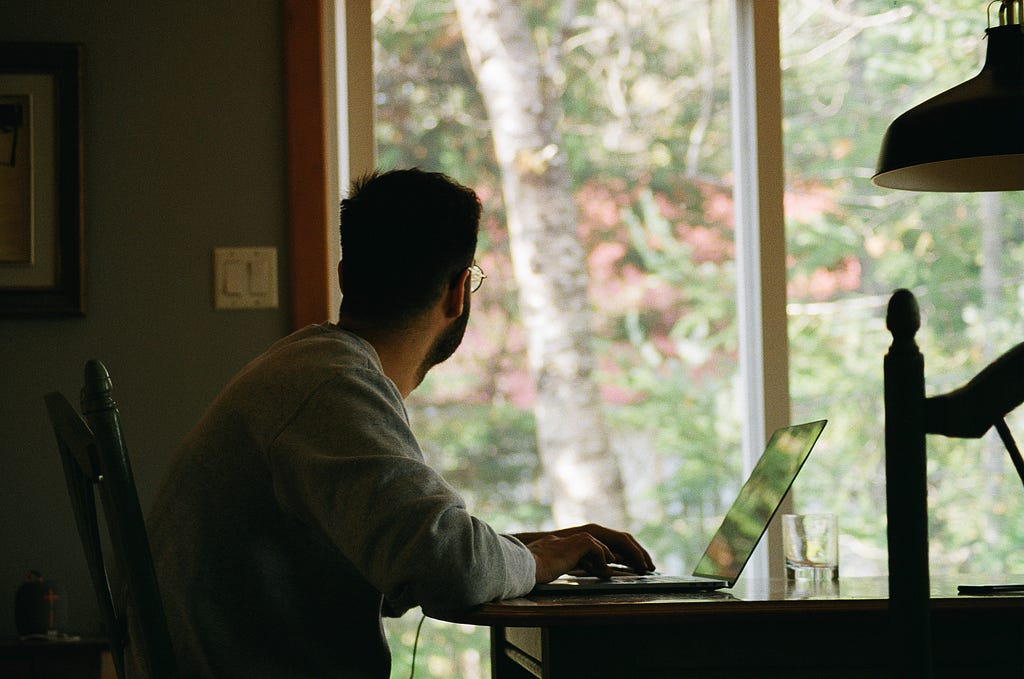 man in front of a laptop on a desk staring out the window