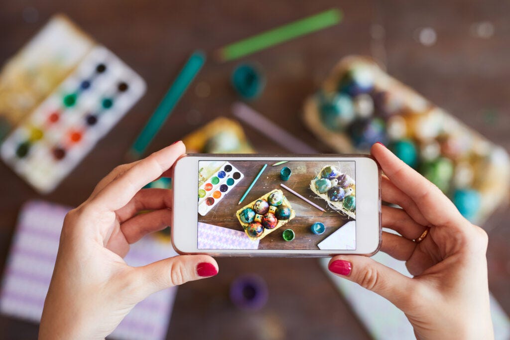 Hands of a Woman holding a phone taking a picture of Easter Crafts — image shows picture of her cellphone screen and the crafts