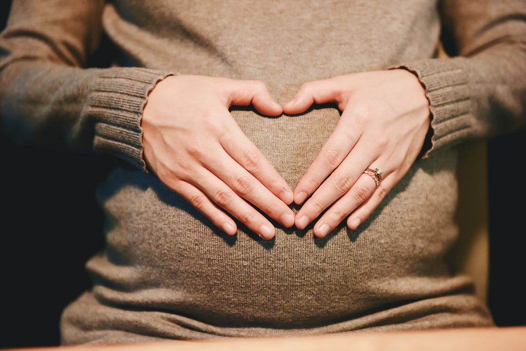 a pregnant woman with fingers on belly making a heart
