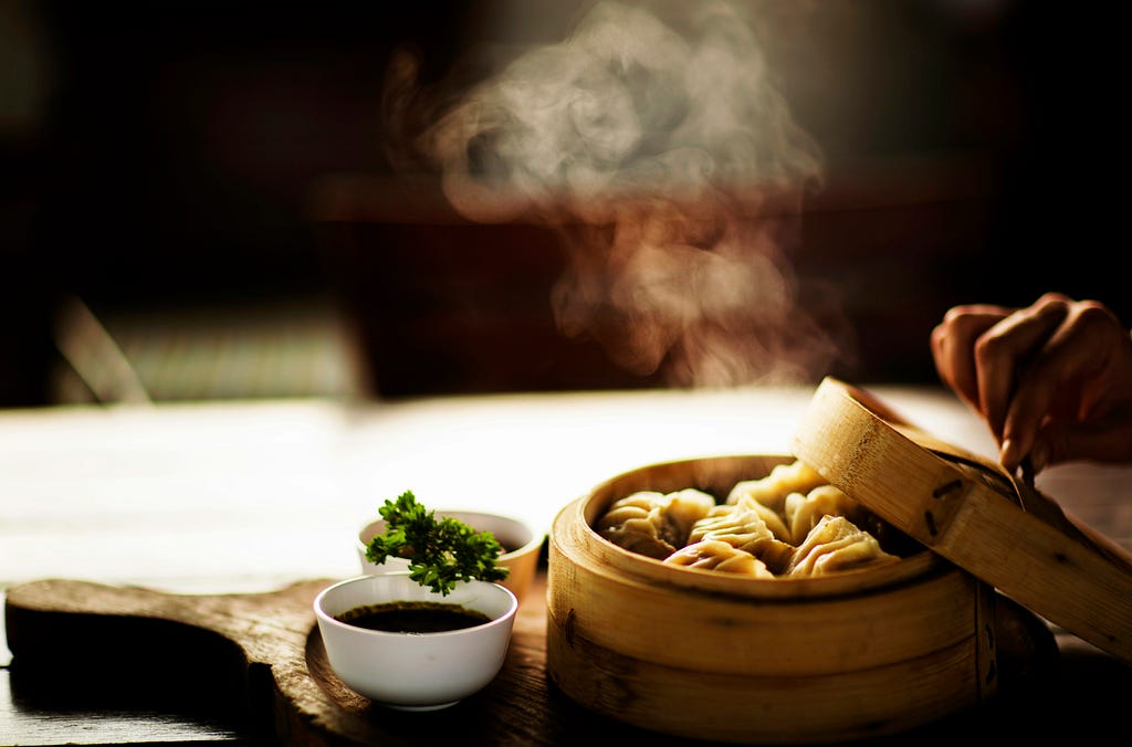 steamed dumplings in a bamboo box and sauces on the side