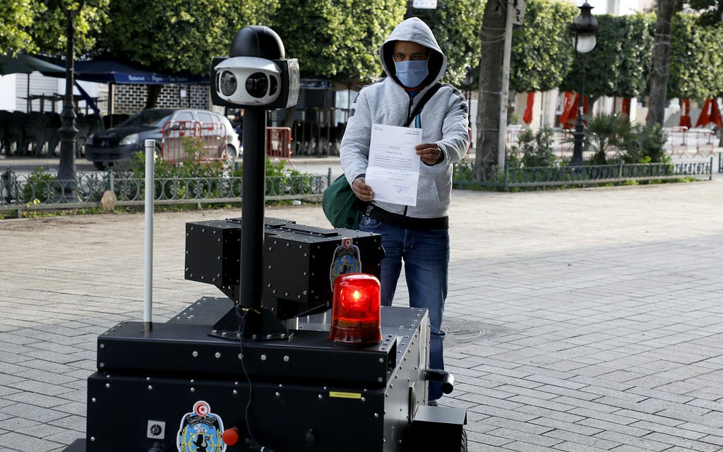 A man holds up a piece of paper to a police robot on a public sidewalk