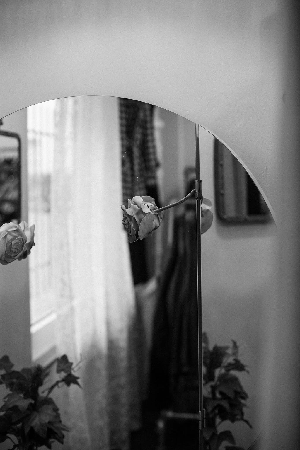 Fotografia em preto e branco de um espelho. No reflexo do espelho estão duas rosas.