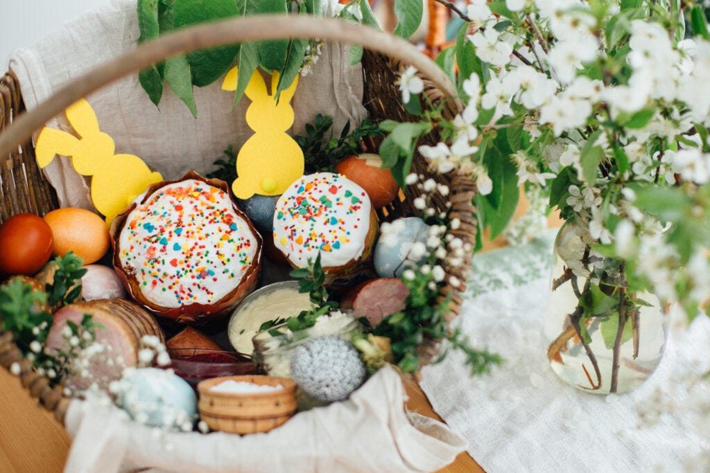 Easter Basket on a table with flowers to the right. The basket is filled with treats and shows the tradition of giving Easter baskets at Easter