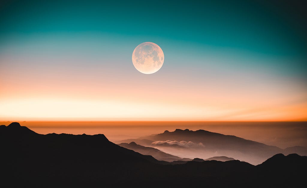 A full moon rises over mountain ridges