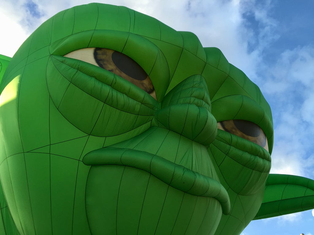 Giant green inflatable Yoda balloon peers out at the world before him.