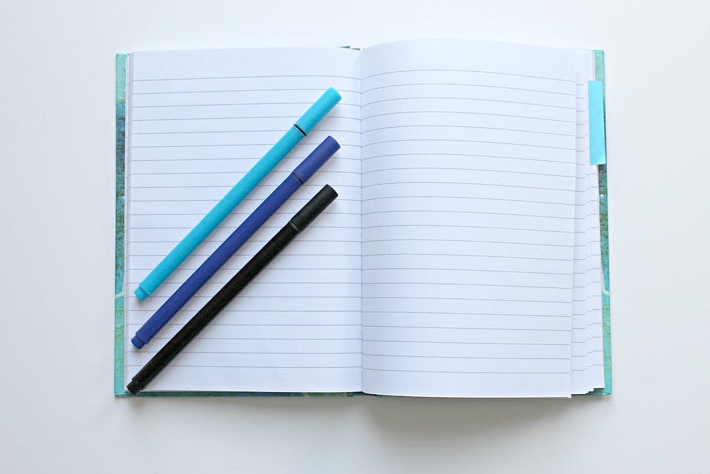 open, blank notebook with pens
