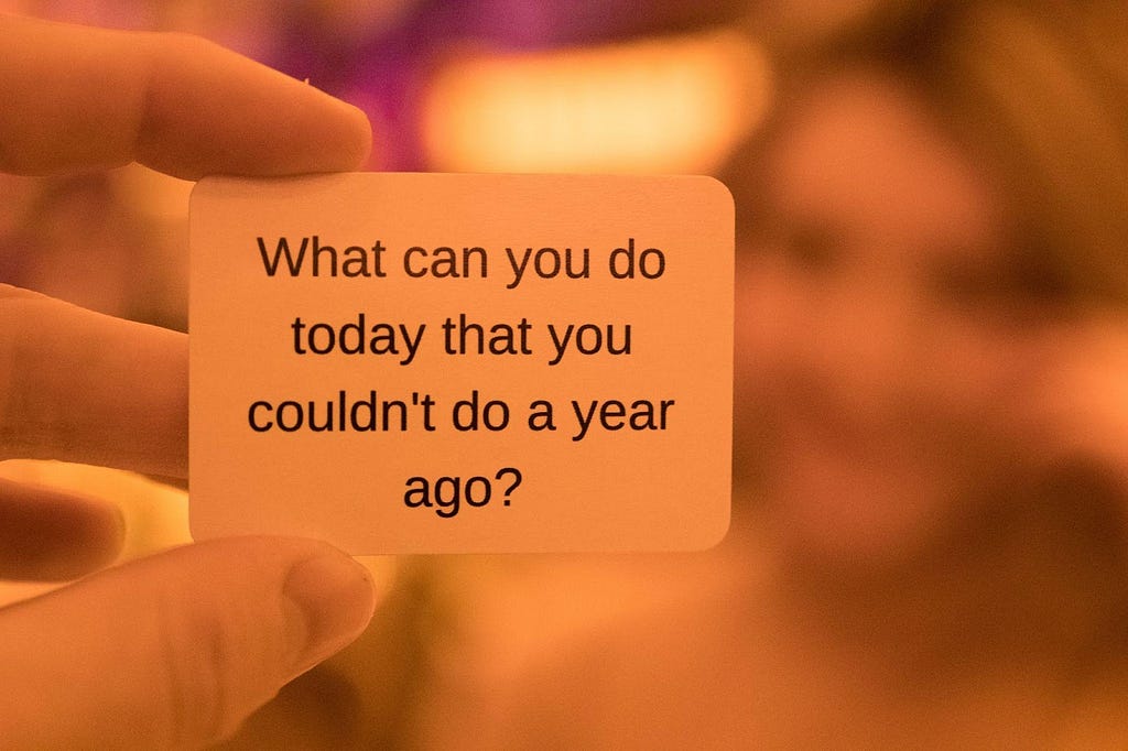 A hand holding a card with the text “What can you do today that you couldn’t do a year ago?”