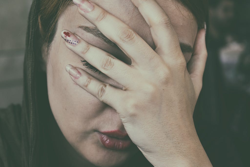 Image of a woman holding a hand in front of her face, as if in pain.