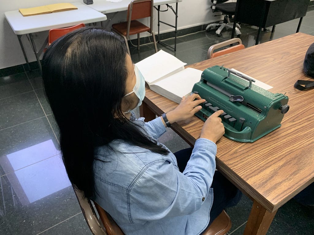 Roxana Alemán sentada escribiendo en Braille ante una máquina Perkins.