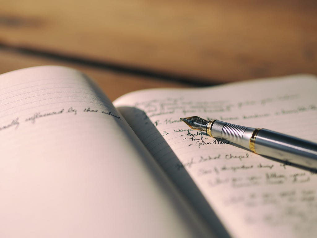a shot of an open journal with a pen across it with writings.