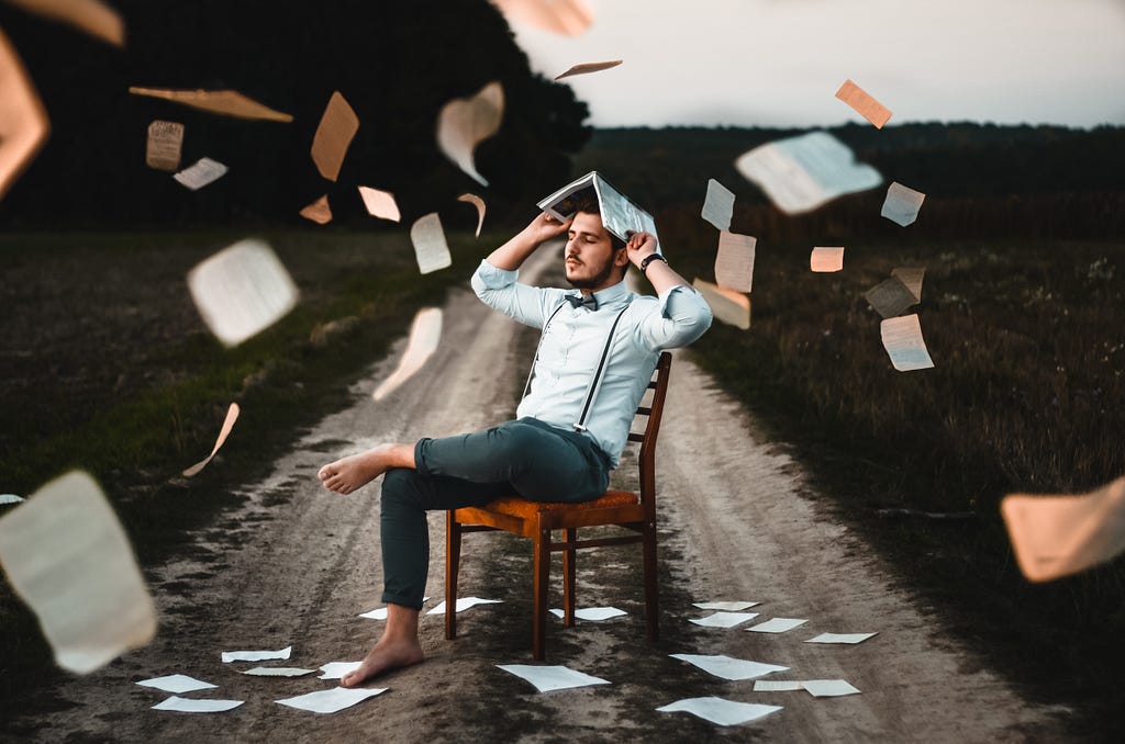 Person sitting on a chair with a book over their head, with papers falling all around them.