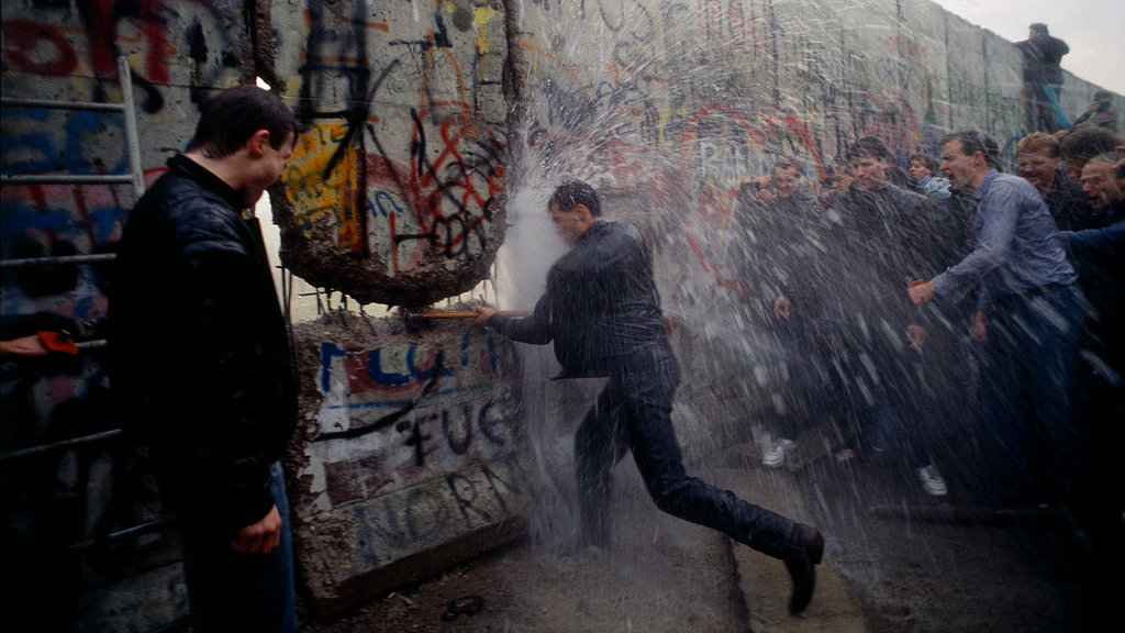 a person breaking down the berlin wall while being sprayed by a fire hose, circa 1989